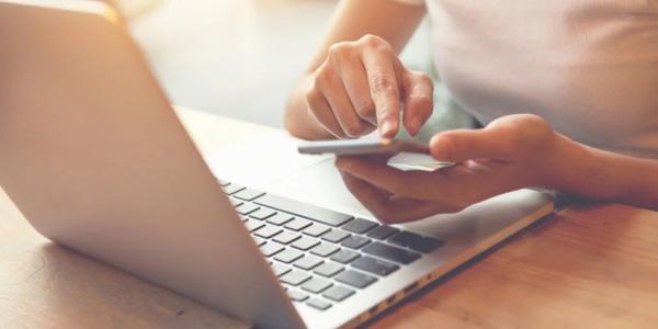 A closeup of a female sitting at a desk holding a mobile device and an opened laptop is placed on the desk.