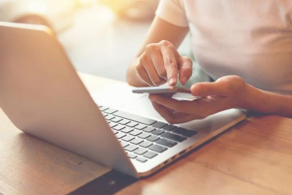 A closeup of a female sitting at a desk holding a mobile device and an opened laptop is placed on the desk.